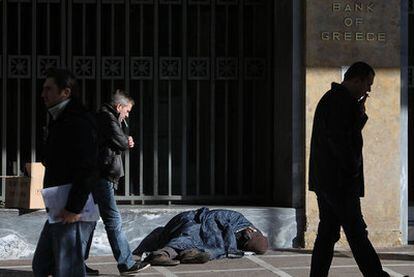 Peatones pasan frente a un vagabundo a las puertas del Banco de Grecia en Atenas.