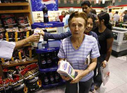 Un empleado de un supermercado de Caracas entrega una caja de leche a cada persona de la cola.