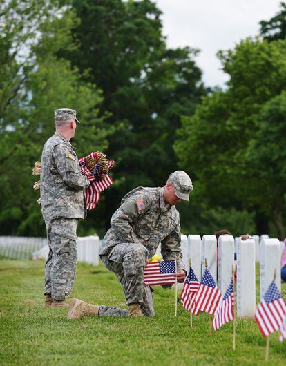 Dos miembros del Tercer Regimiento de Infantería ponen banderas de EE UU frente a las tumbas de soldados caídos en combate.