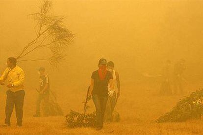 Voluntarios escapan del humo producido en un incendio cerca de Vilarchán.