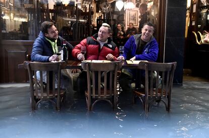 Tres hombres toman una copa de vino en una calle inundada en Venecia.   
