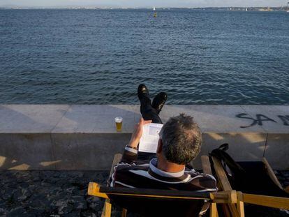 Un hombre lee en la Ribeira das Naus, al lado del río Tajo.