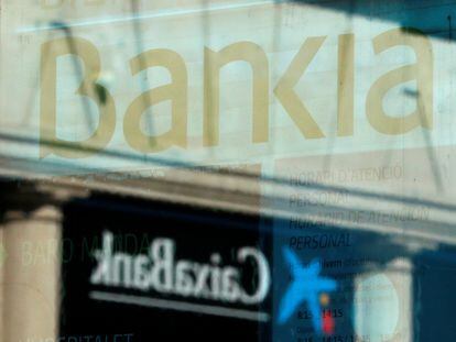 El logo de CaixaBank y el de Bankia se reflejan en el cristal de una sucursal de Barcelona. REUTERS/ Albert Gea