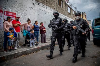 Familias miran a policías armados con máscaras que luchan contra el narcotráfico en la ciudad.