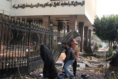 Los manifestantes se protegen tras un improvisado escudo metálico mientras arrojan piedras contra la policía militar que se halla en el interior del Parlamento, en El Cairo.
