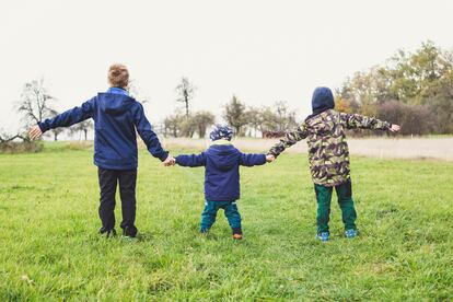 Tres niños se cogen la mano en el campo.