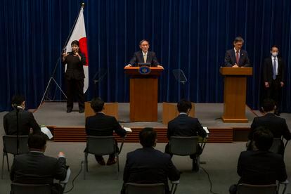 El primer ministro japonés Yoshihide Suga, en el centro, y el responsable del gobierno japonés sobre la pandemia, Shigeru Omi, a la derecha, en una rueda de prensa para actualizar los datos de contagios y medidas en el país nipón