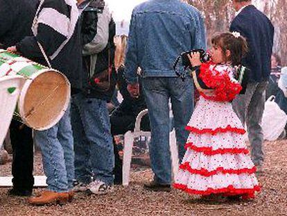 Una niña, ataviada con el traje típico andaluz, bebe agua de su cantimplora.