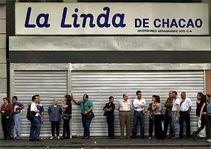 Vecinos de Caracas forman una fila aguardando a poder retirar dinero de un cajero automático junto a un establecimiento cerrado.