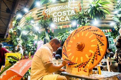 Un artesano trabaja pintando una rueda de carro, de madera. Es un trabajo tradicional en un país que ha apostado por el ecoturismo, y que ha llenado su estand de verde. Dentro se sirven café, zumos y algodón de azúcar.