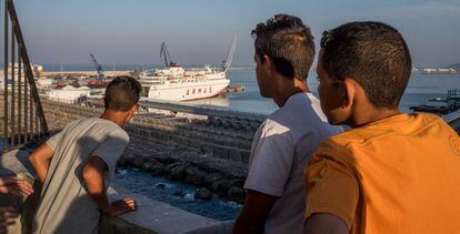 Tres chicos, que viven en la calle, observan los barcos del puerto de Melilla.