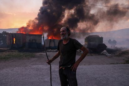 Un hombre delante de su granja mientras arde en un incendio forestal, en Sesklo (Grecia), este miércoles.