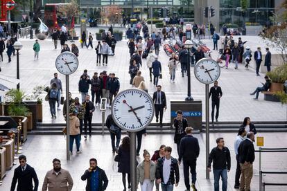 Trabajadores caminando bajo los relojes de Nash Court en el corazón del distrito financiero de Canary Wharf en Londres.