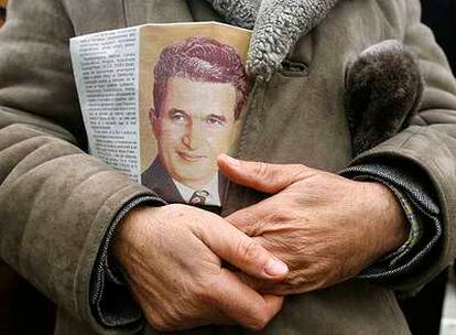 Un hombre sostiene un periódico con la imagen del ejecutado dictador Nicolae Ceausescu ante su tumba, en Bucarest.