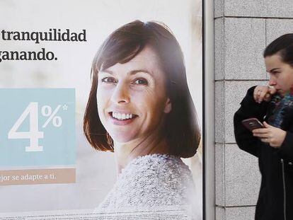 Una  mujer pasea delante de una publicidad de ahorro de un banco. 