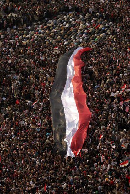 Manifestantes anti-Mubarak ondean una gigantesca bandera egipcia mientras otros rezan en la plaza de la Liberación, en El Cairo.