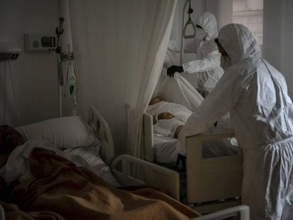 Trabajadores de una funeraria retiran el cuerpo de un anciano fallecido por coronavirus en un asilo mientras otro residente duerme al lado en su cama, en Barcelona.