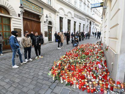 Varios transeúntes ante flores y velas dejadas en homenaje a las víctimas en uno de los puntos del atentado del lunes en Viena.