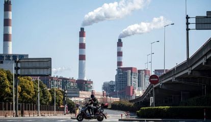 Un motociclista pasa frente a las chimeneas humeantes de una central de generación eléctrica en Shaghái (China).
