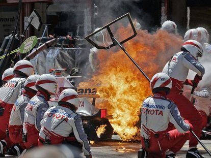 Los operarios apagan las llamas en torno al coche de Jarno Trulli al prenderse la gasolina caída al asfalto.