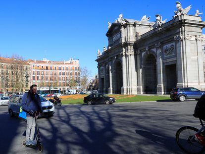 Un hombre circula en un patinete eléctrico por la calzada en la rotonda de la Puerta de Alcalá de Madrid.