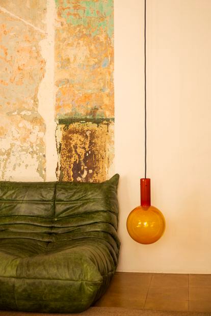 De nuevo las dos grandes señas de identidad de la casa: el verde botella del sofá Togo y la luz. Esta vez se trata de una lámpara de techo en cristal Bolb B de color naranja de la firma The Masie. 