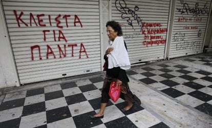 Una mujer camina junto a una tienda cerrada en cuya persiana se puede leer &quot;Cerrado para Siempre&quot;, en el centro de Atenas.