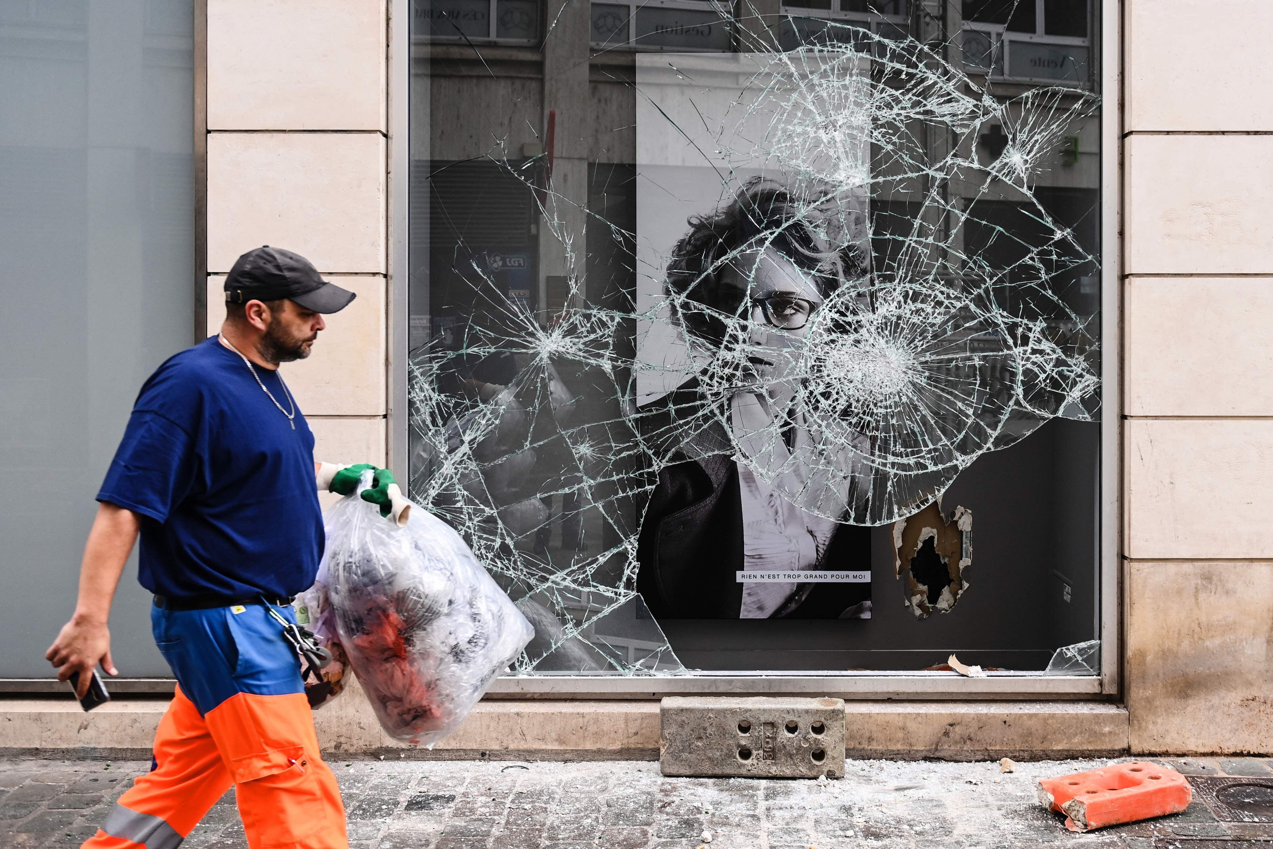 Un empleado municipal pasa junto a un escaparate destrozado durante las protestas en Lyon, este sábado.
