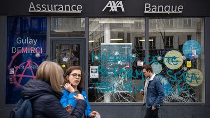 Unos ciudadanos pasan por delante de la sucursal de un banco en París, dañada durante las protestas contra la reforma de las pensiones de Macron, este miércoles.
