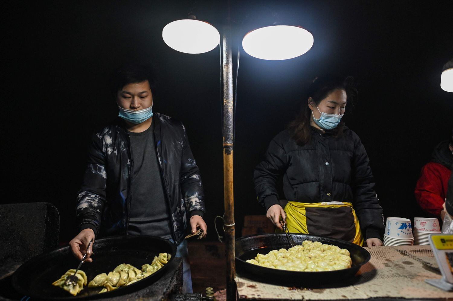 Una pareja con mascarillas prepara alimentos en un puesto de comida callejera en Wuhan.
