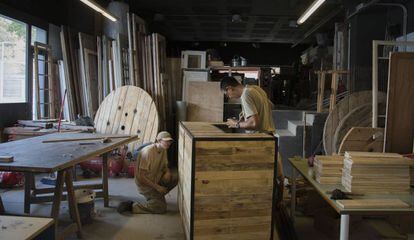Dos empleados pintan una barra de bar en el taller de la tienda barcelonesa L'estoc, que fabrica mobiliario con materiales reciclados.