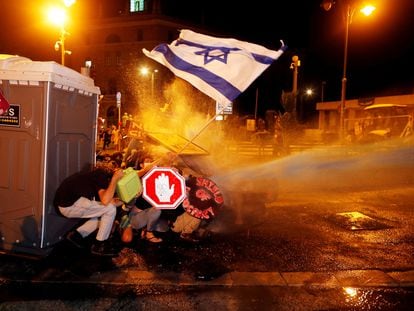 Maniefestantes israelíes se protegen del cañón de agua de la policía durante las protestas en la madrugada del 26 de julio de 2020 en las inmediaciones de la residencia de Benjamín Netanyahu en Jerusalén.