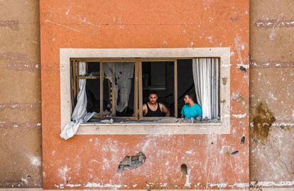Dos hombres miran a través de una ventana dañada en Gaza. 