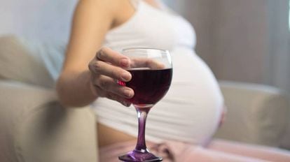 Una mujer embarazada sujeta una copa de vino.