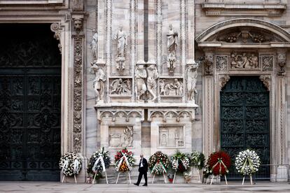 A person walks among several wreaths outside the Milan cathedral.