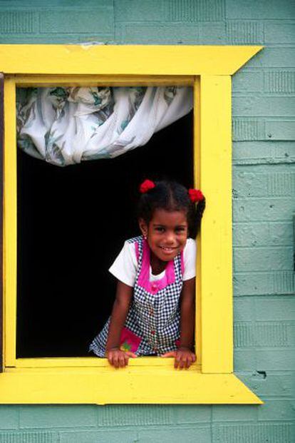 Una niña asomándose a la ventana de una casa de colores, en Curazao.