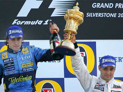 Fernando Alonso levanta una botella de cava mientras Juan Pablo Montoya alza su trofeo de vencedor en el circuito de Silverstone.
