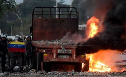 Fuerzas de seguridad venezolanas muestran una bandera junto a camión quemado con ayuda humanitaria. 