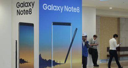 Varias personas utilizando sus teléfonos junto a un cartel publicitario del Galaxy Note 8 de Samsung. 