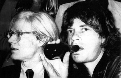 El líder de los Rolling Stones, Mick Jagger, bebe un refresco en compañía del artista Andy Warhol (izda), durante la promoción de su nuevo disco 'Love You Live', el 24 de septiembre de 1977.