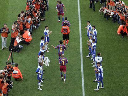 Los jugadores del Espanyol hacen pasillo a los del Barça en homenaje al campeón antes del inicio del partido.