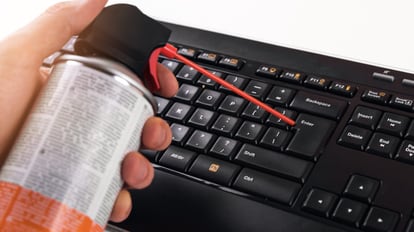 Una mano sostiene un frasco de aire comprimido con el que limpia las ranuras de un teclado.
