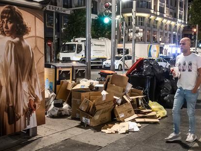 Un hombre pasa delante de varias cajas de cartón junto a los contenedores en la Gran Vía de Madrid, este sábado.