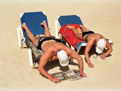 Una pareja trata de leer en una postura incómoda mientras toma el sol en una playa de Mallorca.