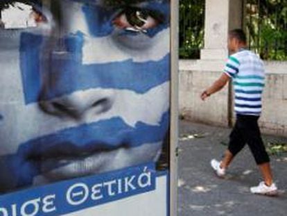 Un peatón pasa delante de un cartel que invita a votar a los griegos