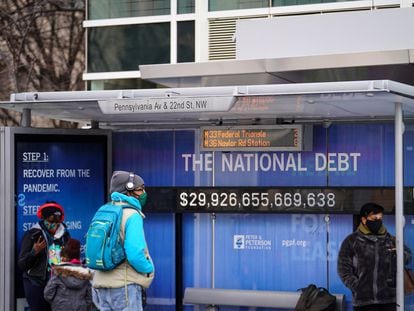 Varias personas en una parada de autobús con una pantalla que muestra el registro de la deuda pública, este lunes en Washington.