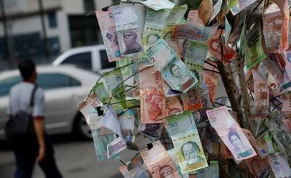 Un hombre pasa frente a billetes de bolívar tendidos en una calle de Caracas.