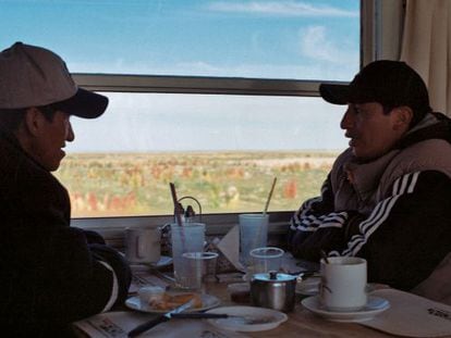 Dos bolivianos conversan en uno de los trenes que atraviesa el altiplano, con campos de quinua coloreándose al fondo.