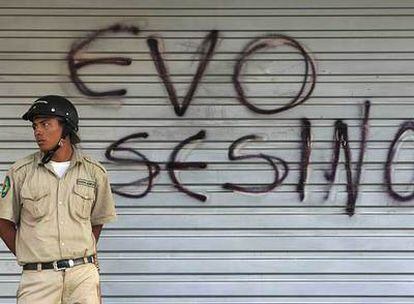 Un policía de Santa Cruz hace guardia ante una pintada contra el presidente de Bolivia.