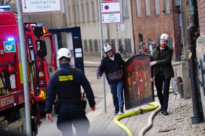 Dos operarios recogen una de las obras de arte del interior del edificio incendiado este martes en Copenhague. 